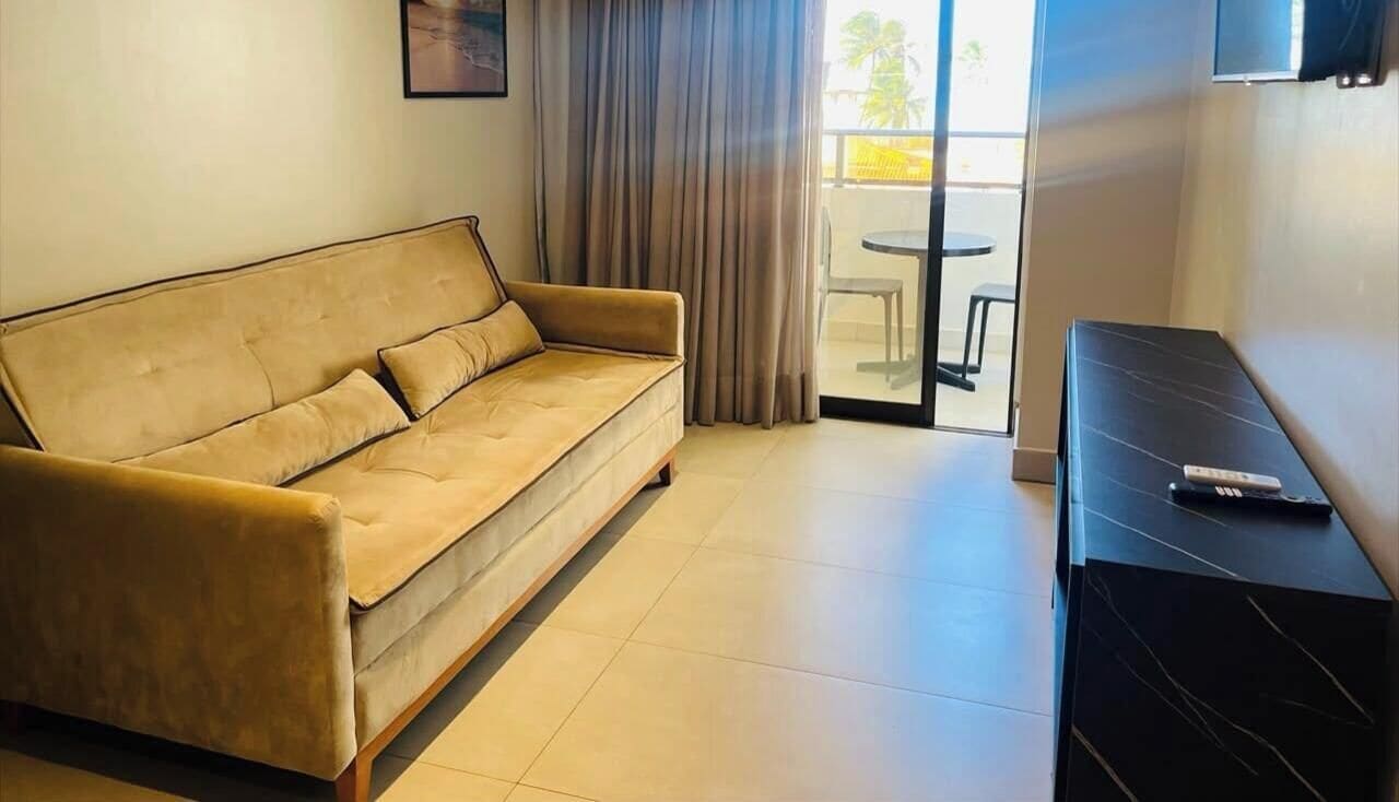 A room with a sofa, a TV on a stand, and a view of the outside.
