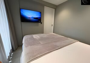 Un dormitorio con una cama, televisión instalada en la pared y una puerta.