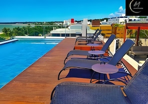 A rooftop pool area with lounge chairs and tables, a clear view of the sea, and buildings in the background. - LM INFINITY CABO BRANCO (João Pessoa)