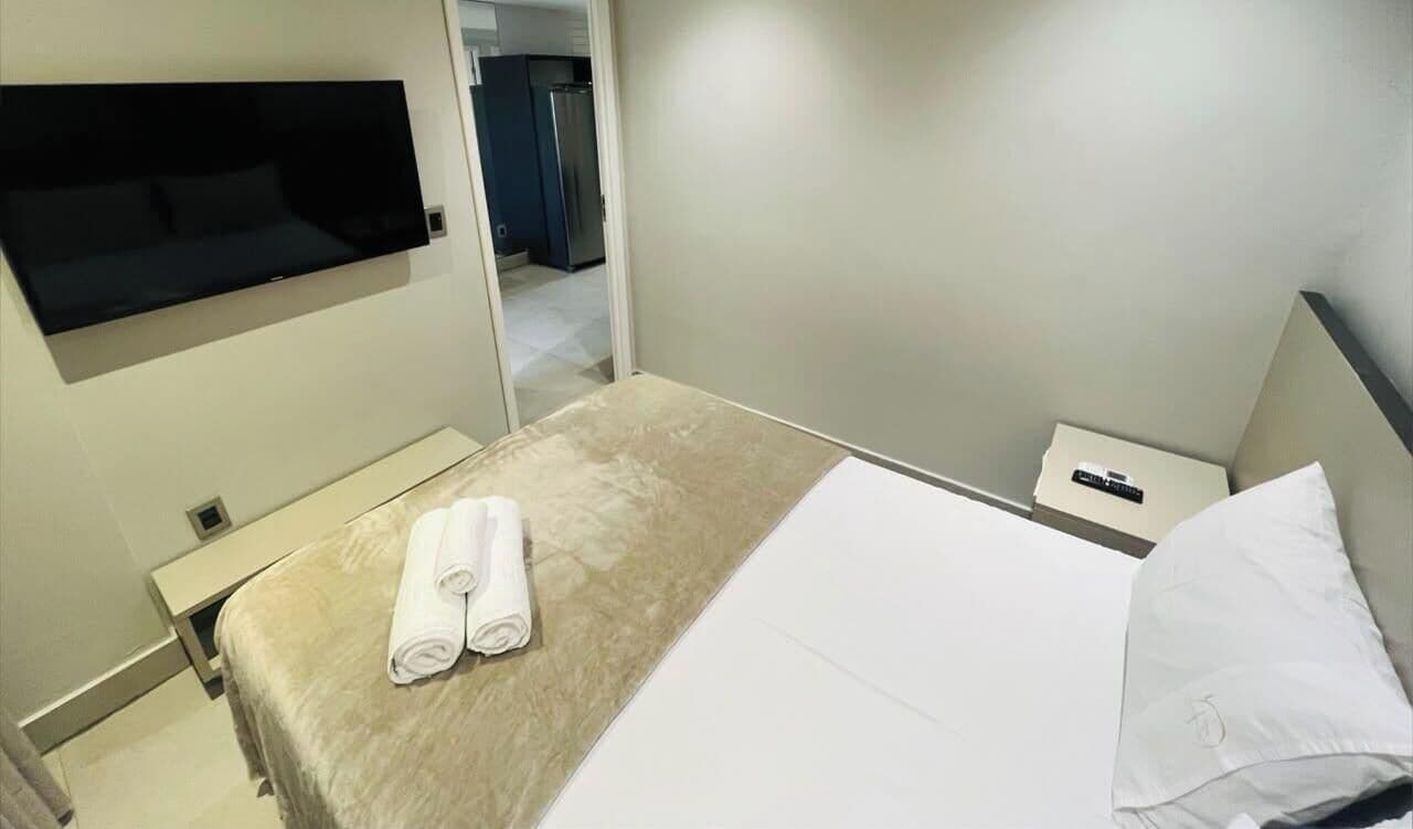 Une chambre d’hôtel comprenant un lit, un téléviseur à écran plat fixé au mur, une table de chevet avec une télécommande et une porte donnant accès à une salle de bain.