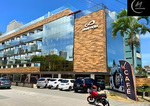 A modern building with a glass facade, a wooden-textured wall, and a sign for 'Unity Cafe.' - LM INFINITY CABO BRANCO (João Pessoa)