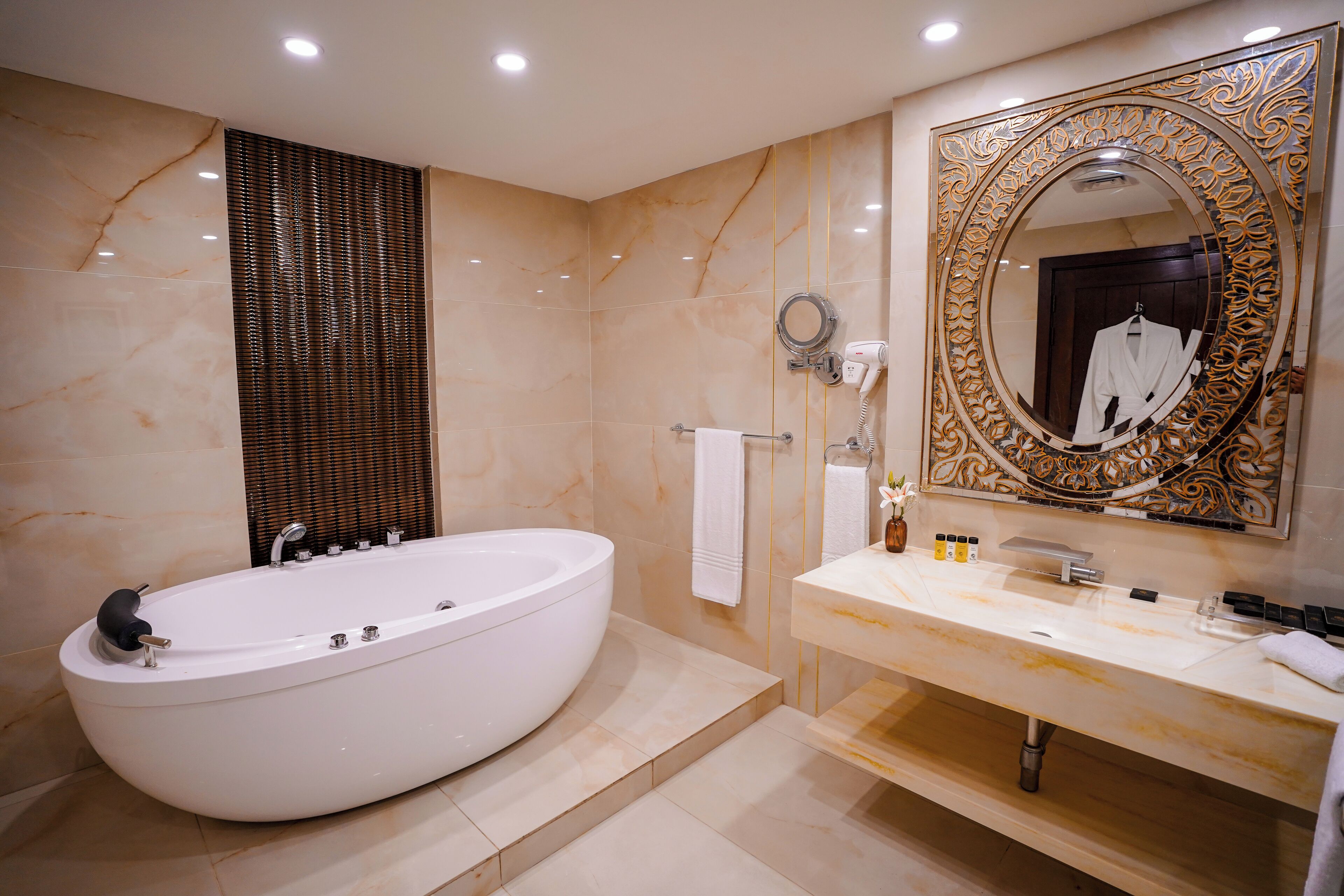 Un baño moderno con una bañera independiente, un espejo grande con un marco decorativo y un mueble de tocador con un perchero para toallas.