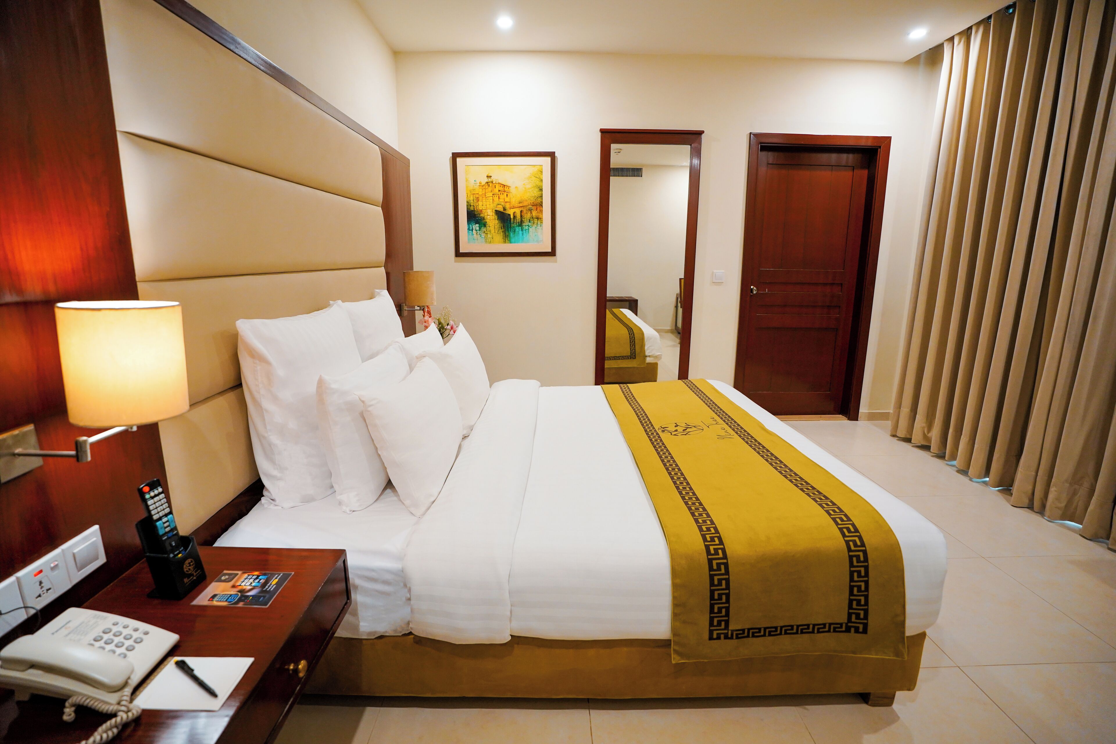 A hotel room with a large bed, a bedside table with a lamp, a phone, and a painting on the wall.