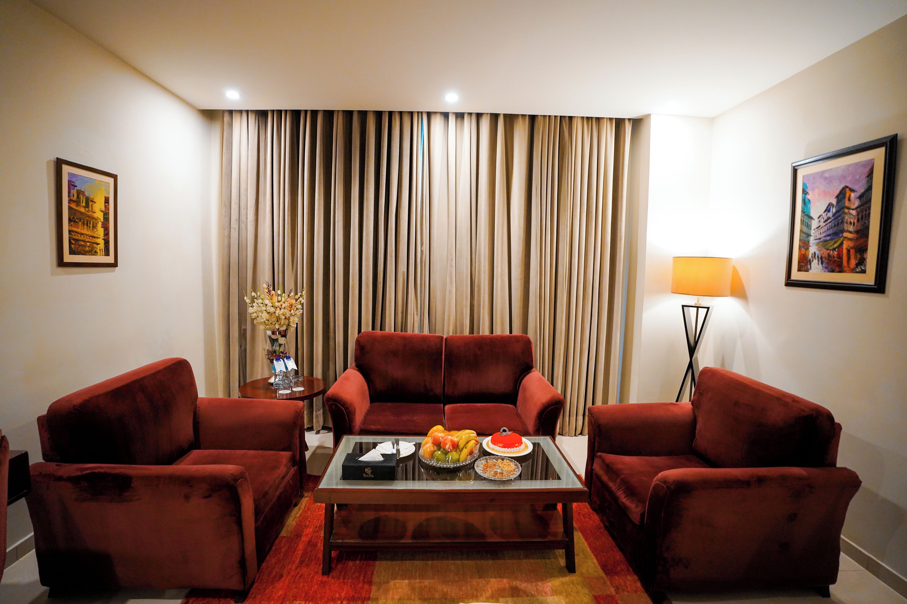 A living room with a red sofa set, a glass coffee table, and a dining table with fruit and a red plate.
