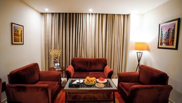 A living room with a red sofa set, a glass coffee table, and a dining table with fruit and a red plate.
