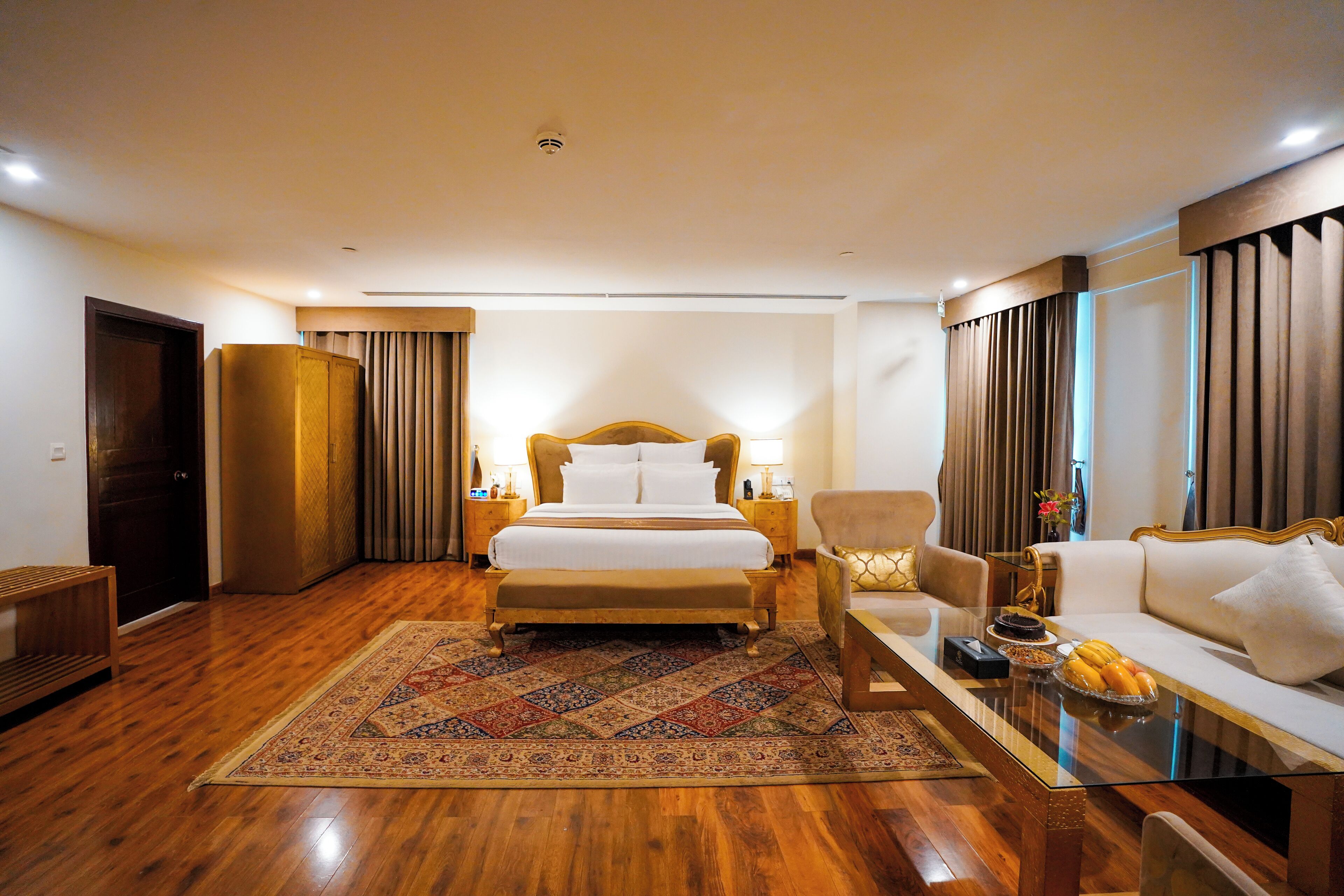 A hotel room with a large bed, a sofa, a coffee table, and a wooden floor.