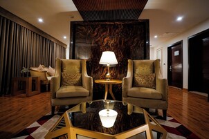 A lobby with two armchairs, a glass coffee table, a lamp, and a marble wall.