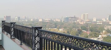 Un balcón con barandillas negras ornamentadas que da a una vista urbana con diversos edificios y zonas verdes.