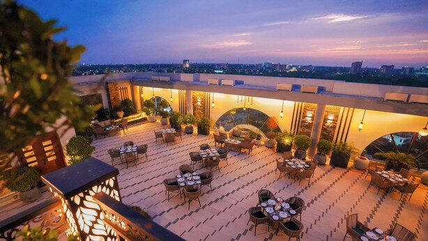 A rooftop terrace with multiple dining tables and chairs, surrounded by potted plants and illuminated by hanging lights. - Nine Tree Luxury Hotel & Suites (Lahore)