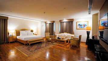 A hotel room with a large bed, a sofa, a chair, a coffee table, and a TV.