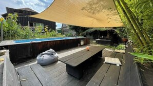 Une terrasse en bois avec une piscine, un espace barbecue et un coin salon ombragé.