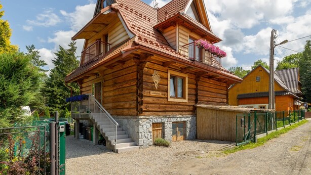 A wooden log cabin with a stone foundation, a balcony with flowers, and a staircase leading to the entrance. - Family Apartment in Zakopane | Parking | Air Conditioning (Zakopane)