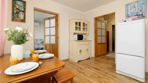 A dining area with a wooden table set for two, a white refrigerator, a microwave, and a cabinet with glass doors. - Family Apartment in Zakopane | Parking | Air Conditioning (Zakopane)