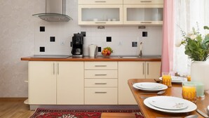 A modern kitchen with white cabinets, a stainless steel range hood, and a wooden countertop. There is a dining table set with plates, glasses, and a fruit bowl. - Family Apartment in Zakopane | Parking | Air Conditioning (Zakopane)
