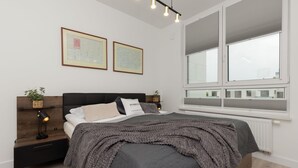 Un dormitorio moderno con una cama grande, mesitas de noche, un velador y una ventana con persianas, además de cuadros en la pared.
