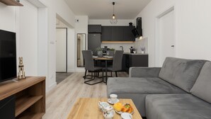 Una sala de estar moderna con un sofá gris, una mesa de centro de madera con tazas de té y un televisor sobre un mueble de madera.