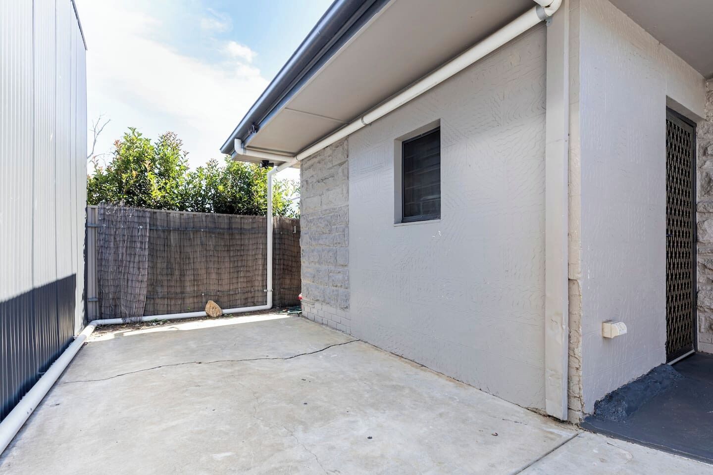 Un immeuble résidentiel doté d’un patio en béton, d’une petite fenêtre et d’une porte avec une grille en métal.