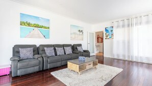Een moderne woonkamer met een grijze bank, decoratieve kussens, een houten salontafel en kunstwerken aan de wanden.