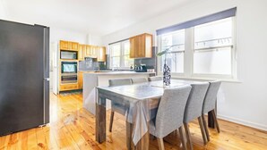 Een moderne keuken met houten kastjes, een eethoek met een tafel en stoelen, en een groot raam dat voor natuurlijk licht zorgt.