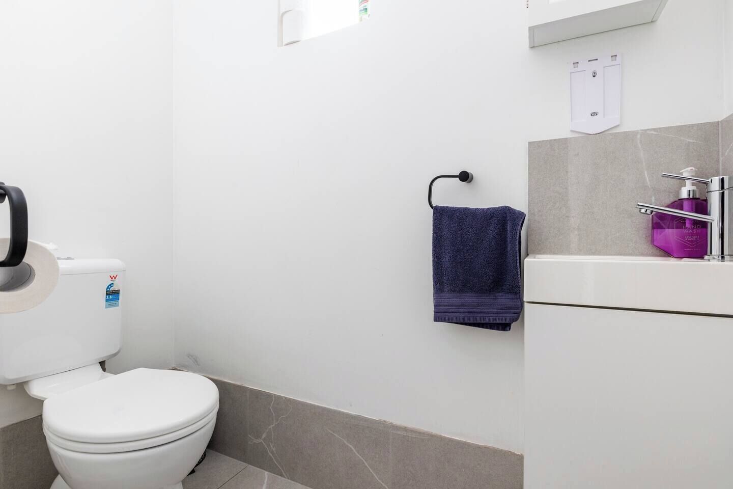 A bathroom with a toilet, a towel rack, a hand wash dispenser, and a soap dispenser.