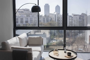 A modern living room with a large window, a sofa, a coffee table, and a lamp.