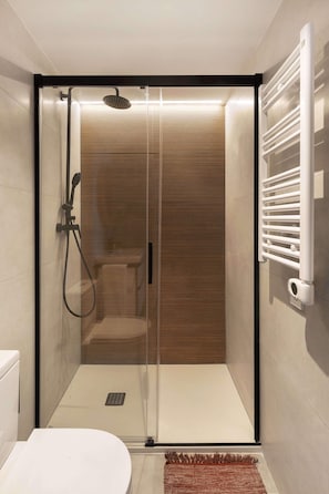 A modern bathroom with a glass-enclosed shower, a white toilet, and a towel rack. - The Bright Oasis - Design 1 BR unit in Poble Nou (Barcelona)
