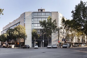 A modern building with a glass facade, parked cars, and trees.