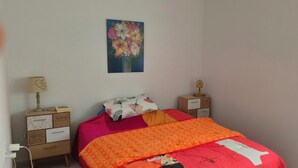 A bedroom with a bed, a nightstand, a lamp, a painting, and a window.