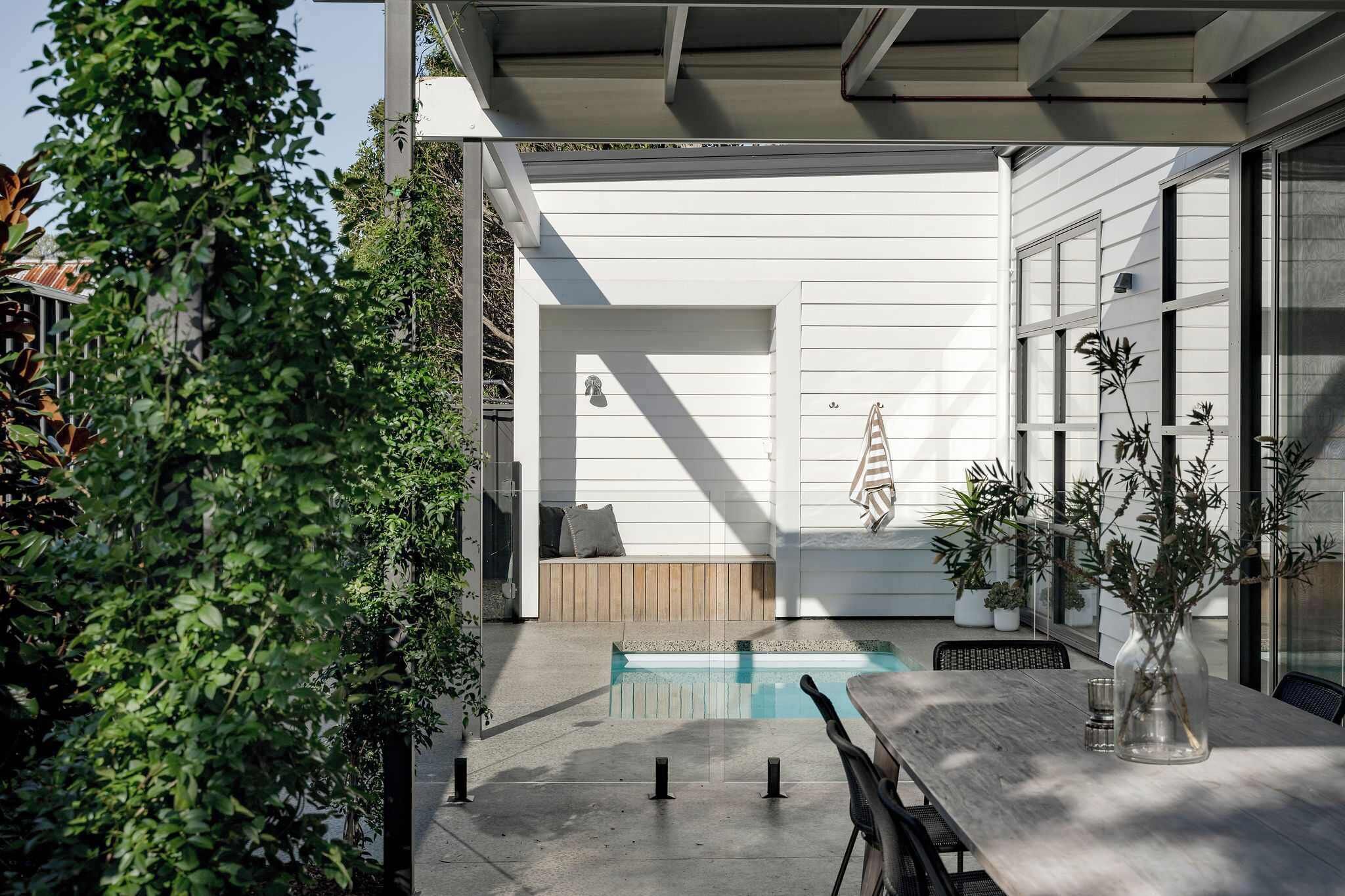 Un patio moderno al aire libre con piscina, zona de estar y plantas en macetas.