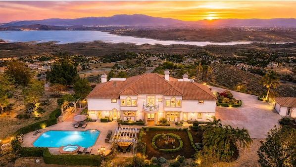 A large house with a swimming pool, surrounded by landscaped gardens and a view of a lake and mountains.