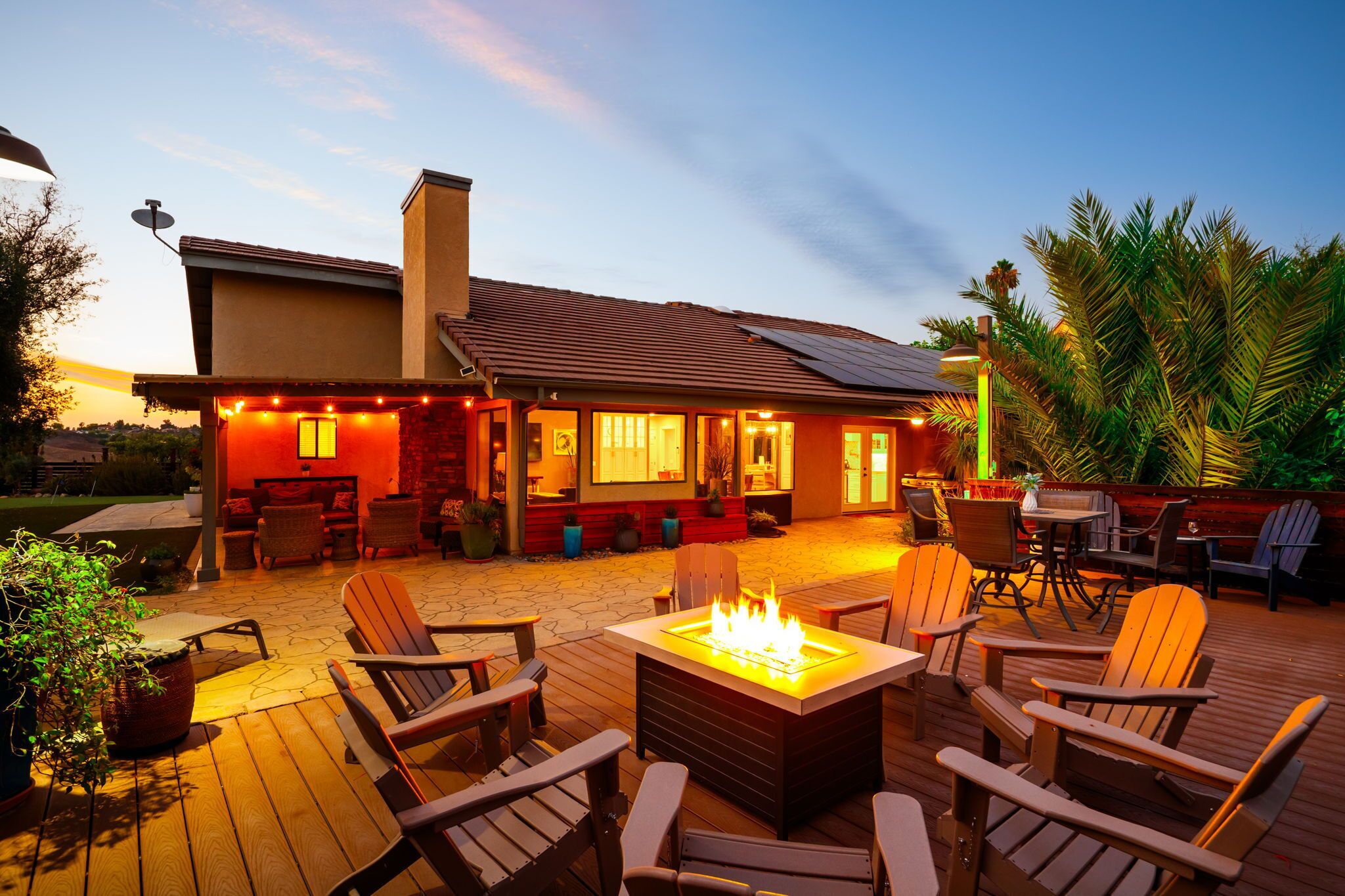 A patio area with outdoor seating, a fire pit, and a building with a tiled roof and solar panels.