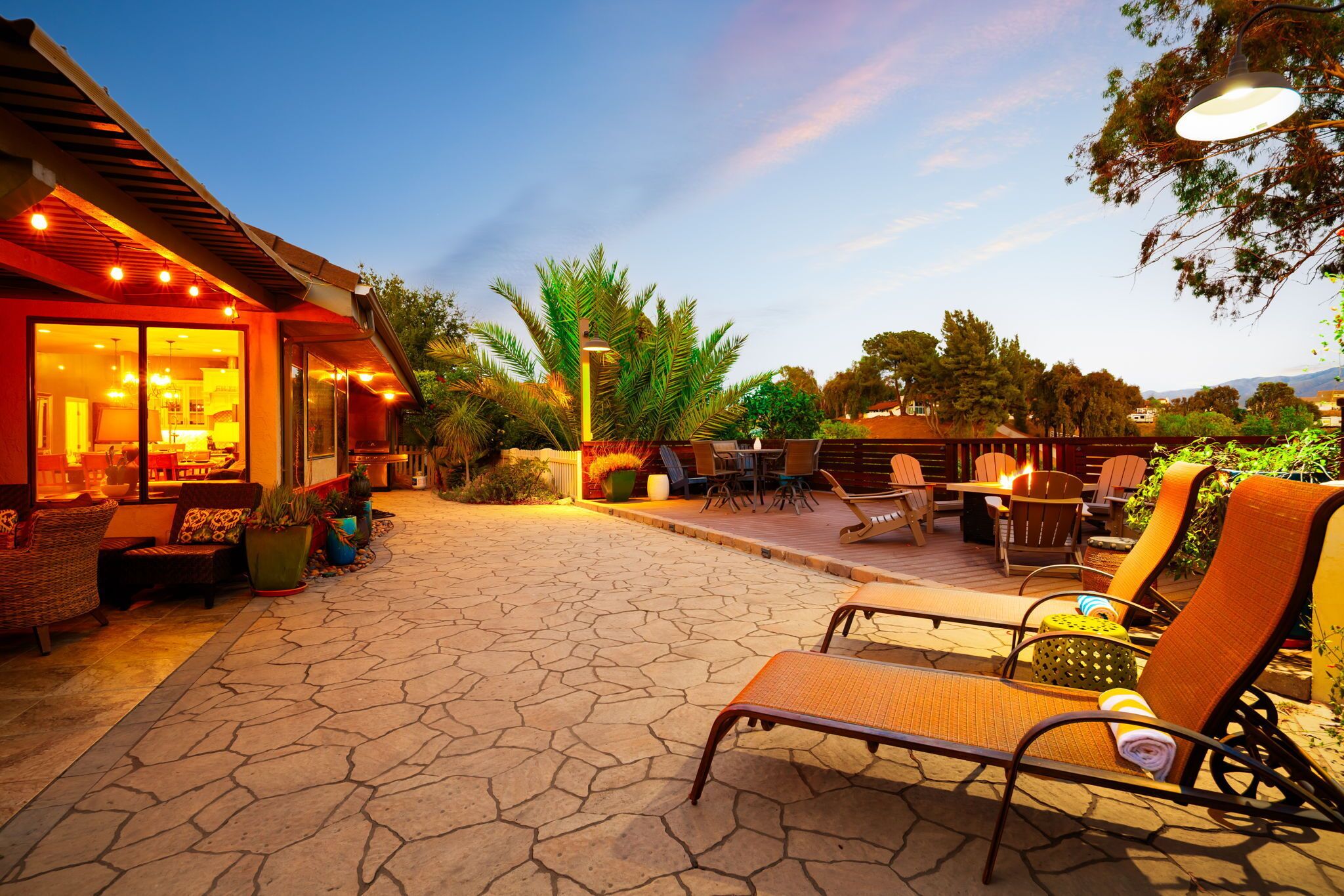 An outdoor patio area with stone flooring, outdoor seating, and a building with large windows and lights.
