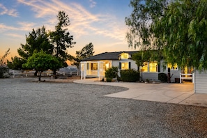 A single-story house with a covered porch, a gravel driveway, and surrounding trees.