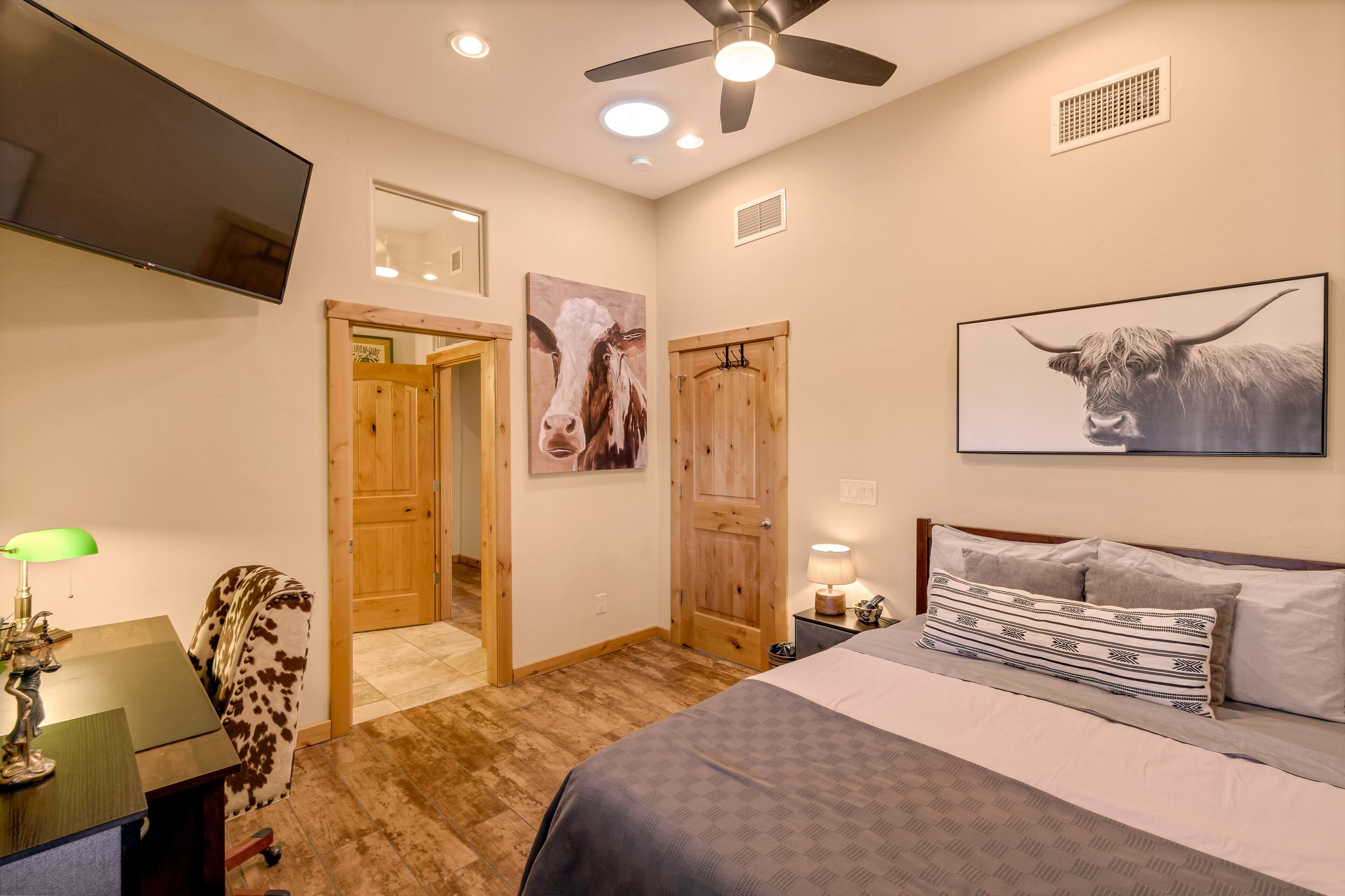 A bedroom with a bed, a desk, a chair, a TV, and artwork on the walls.