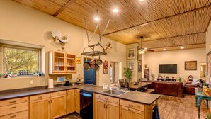 A spacious kitchen with wooden cabinets, a dishwasher, and a dining area with a leather couch and a TV. - La Puerta Azul- Stunning Desert Retreat; Pool/Spa (Tucson)