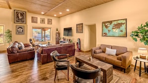 A spacious living room with leather sofas, a wooden coffee table, and a large world map on the wall. - La Puerta Azul- Stunning Desert Retreat; Pool/Spa (Tucson)