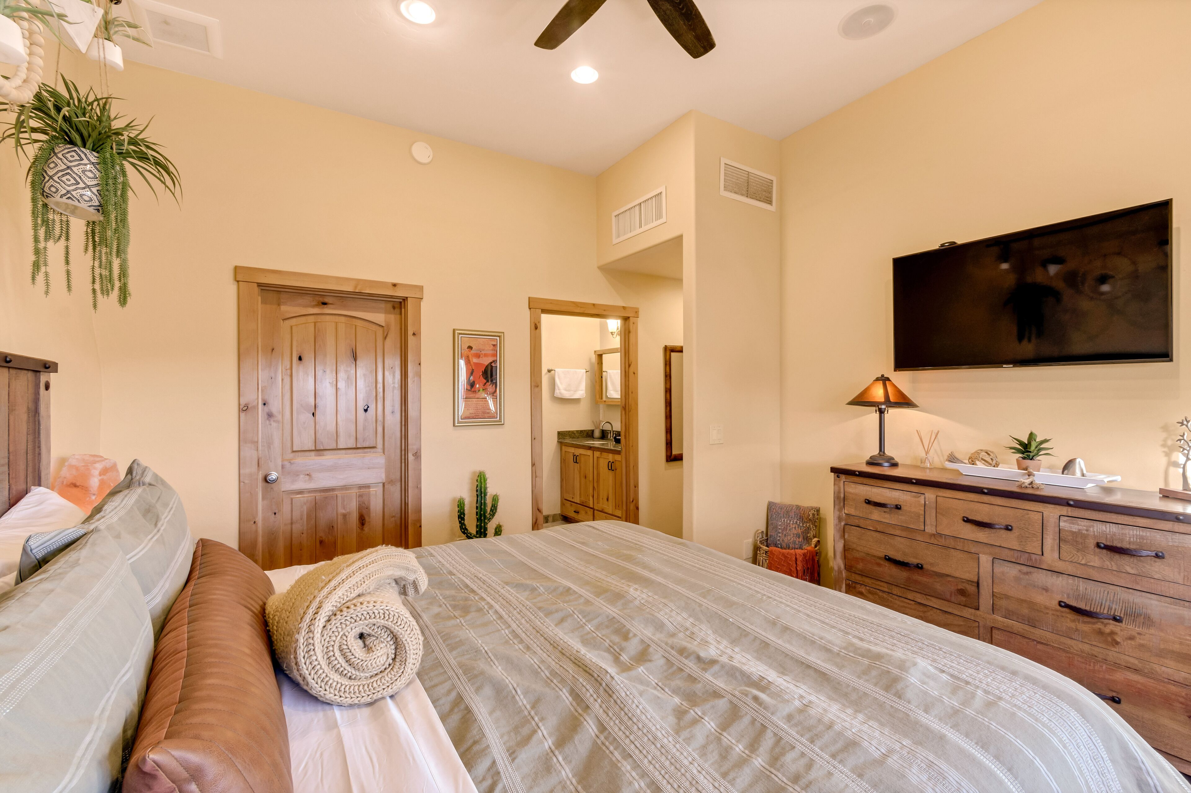Un dormitorio con una cama grande, un aparador de madera y un televisor montado en la pared.