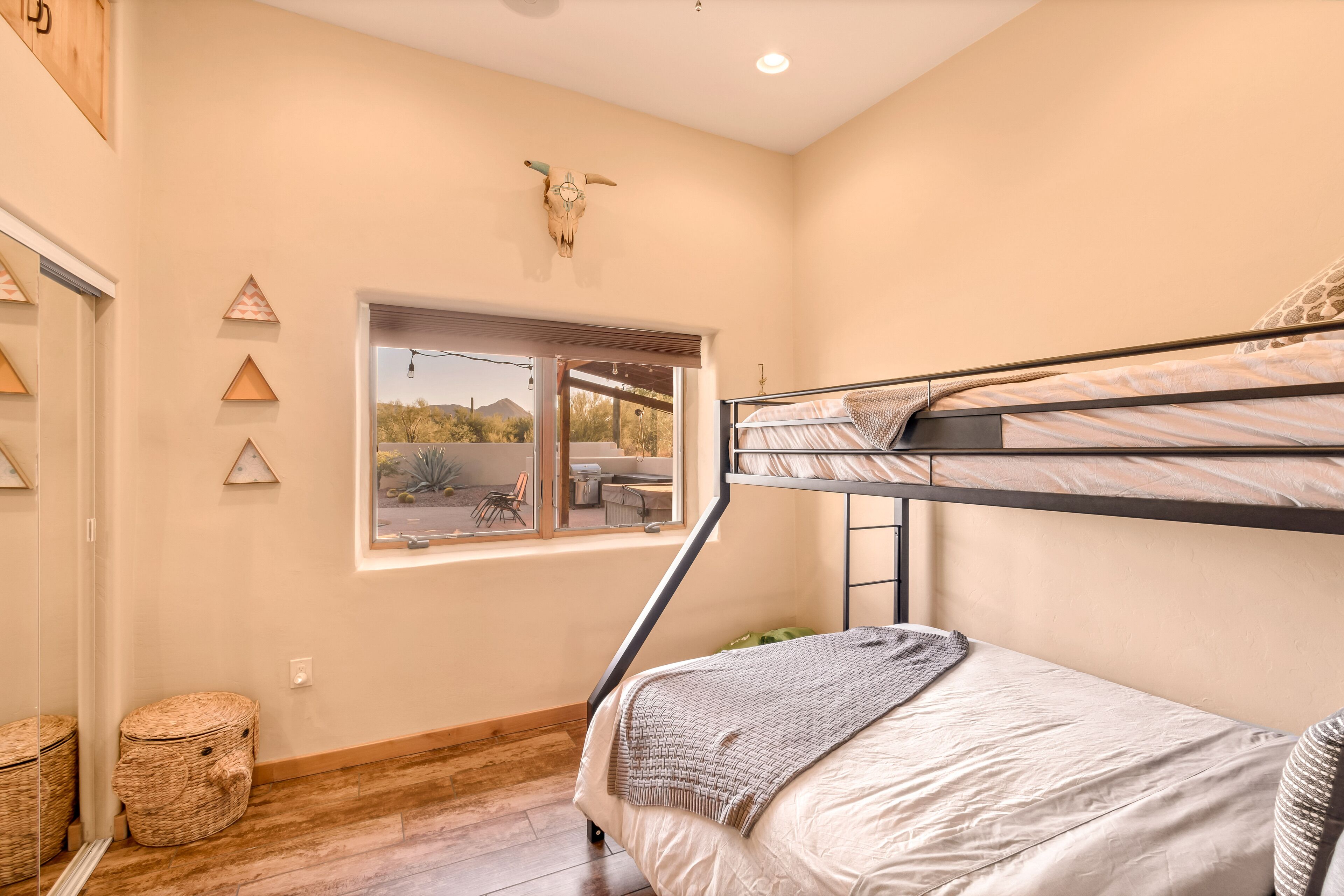 A bedroom with a bunk bed, a window with a view of the outdoors, a decorative skull on the wall, and a woven basket.