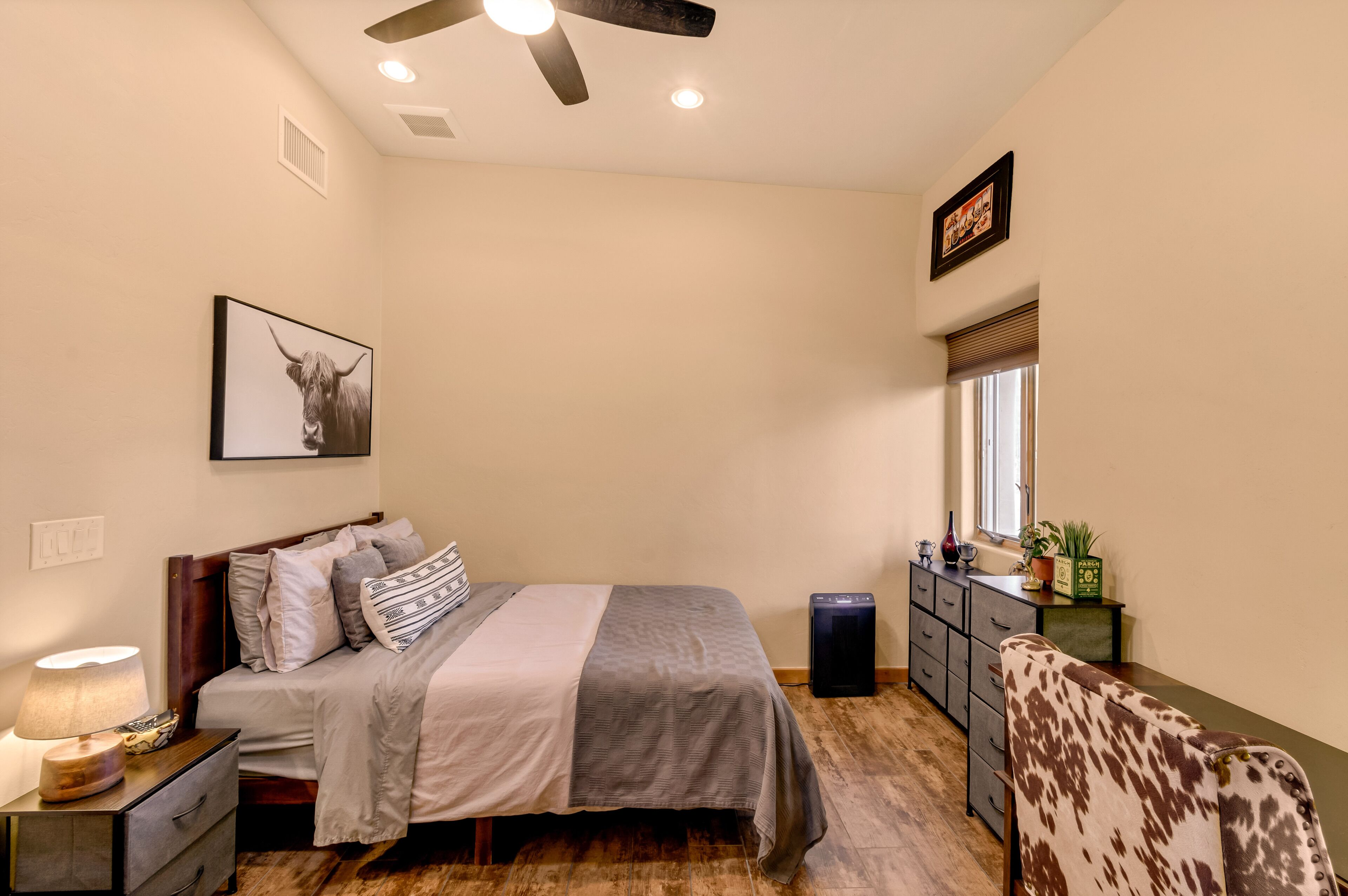 Ein Schlafzimmer mit Bett, Nachttisch, Lampe, Kommode und Deckenventilator.
