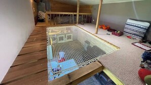 Een kamer met een houten vloer, een stapelbed, een klein omheind speelgedeelte met een gaashek en een vloerbedekking.