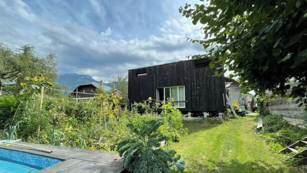 Een modern huis met een zwembad, omgeven door weelderige begroeiing en een bewolkte lucht.