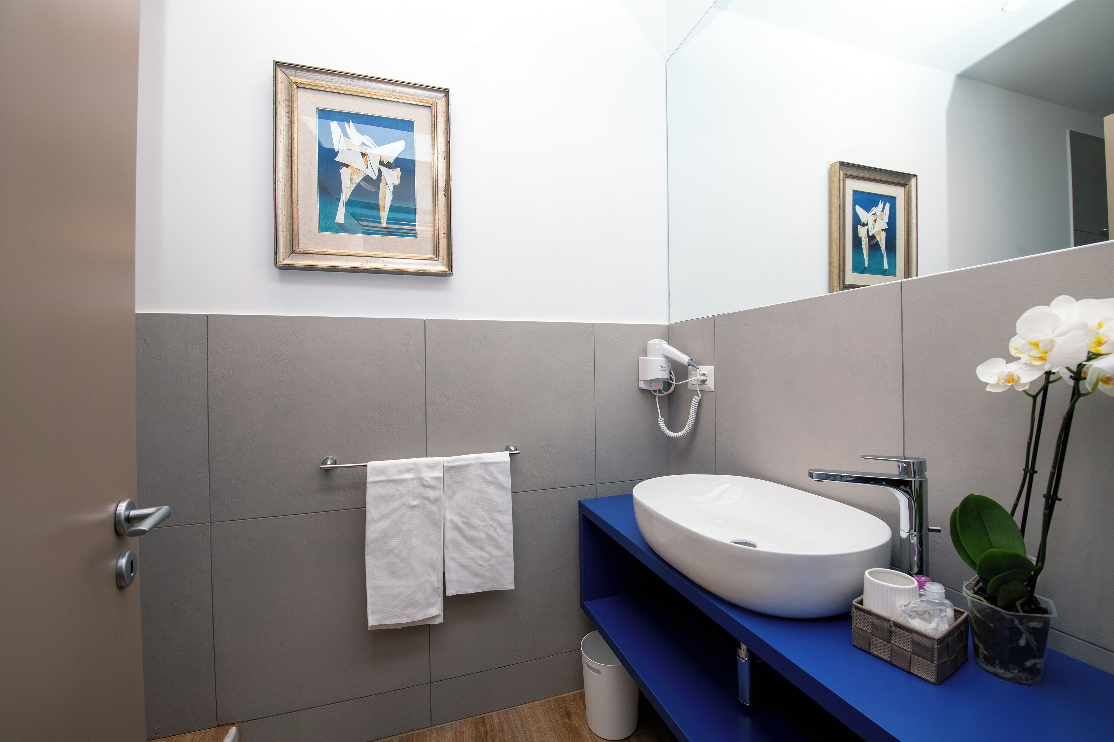 Ein modernes Badezimmer mit einem weißen Waschbecken, einer blauen Ablage und einem gerahmten Bild an der Wand.