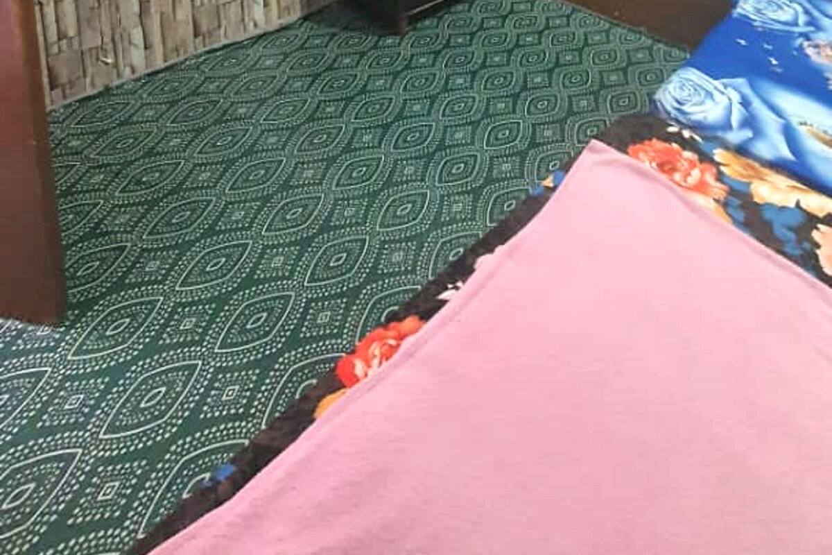 A room with a television mounted on the wall, a wooden headboard, a bed with a patterned bedspread, and a small wooden cabinet.