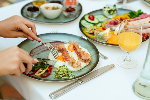 Una mesa de desayuno con platos de comida, un vaso de zumo de naranja y un tenedor.