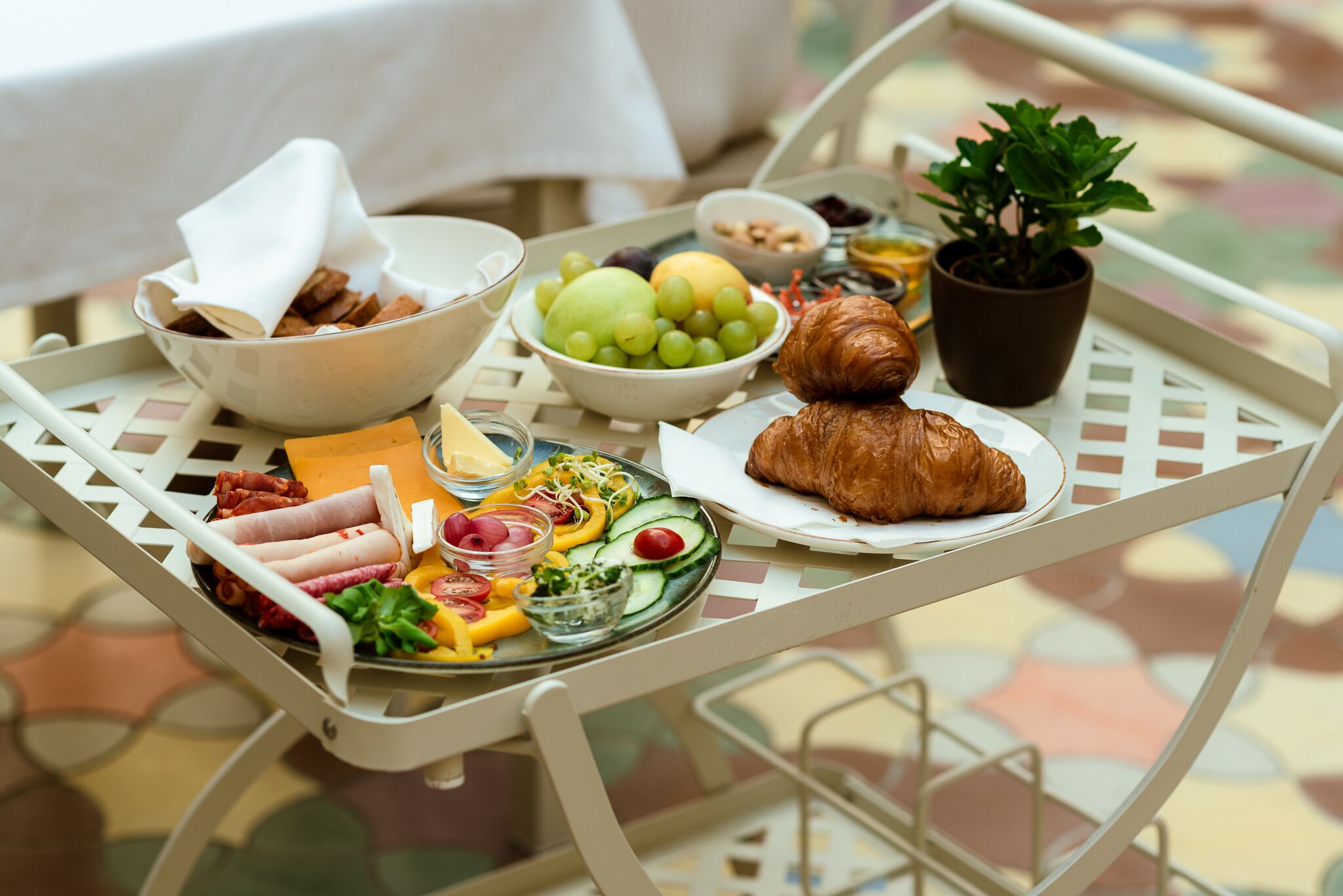 Un plateau de petit-déjeuner contenant divers aliments, notamment de la viande, du fromage, des fruits et un croissant, posé sur une table en métal blanc.