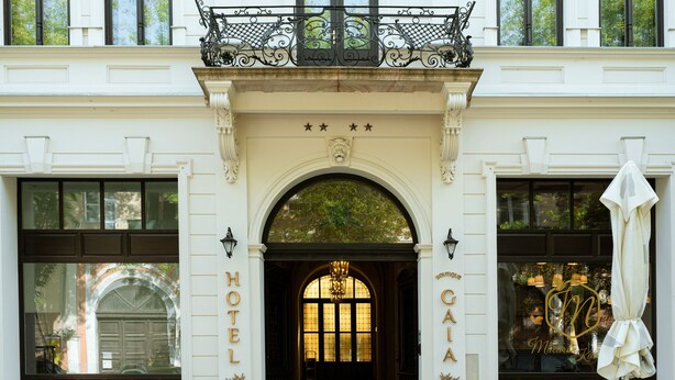 L’entrée d’un hôtel, avec une grande arche, de larges fenêtres et un balcon orné de balustrades en fer forgé.