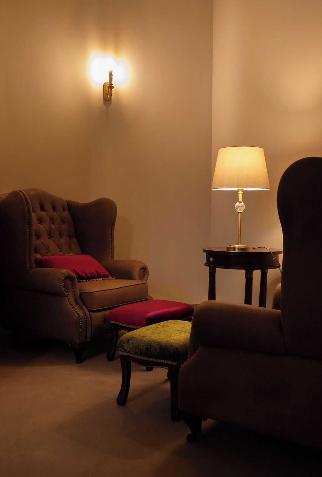 Une pièce chaleureuse avec un fauteuil à capitons, un pouf assorti et une table d’appoint sur laquelle se trouve une lampe.