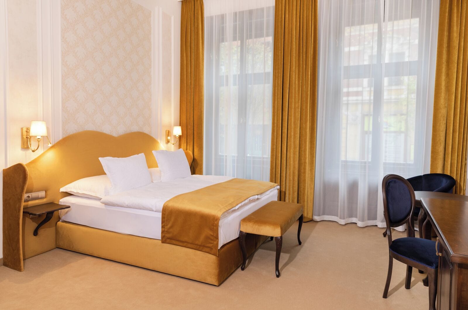 A hotel room with a bed, bedside tables, a desk, and chairs.