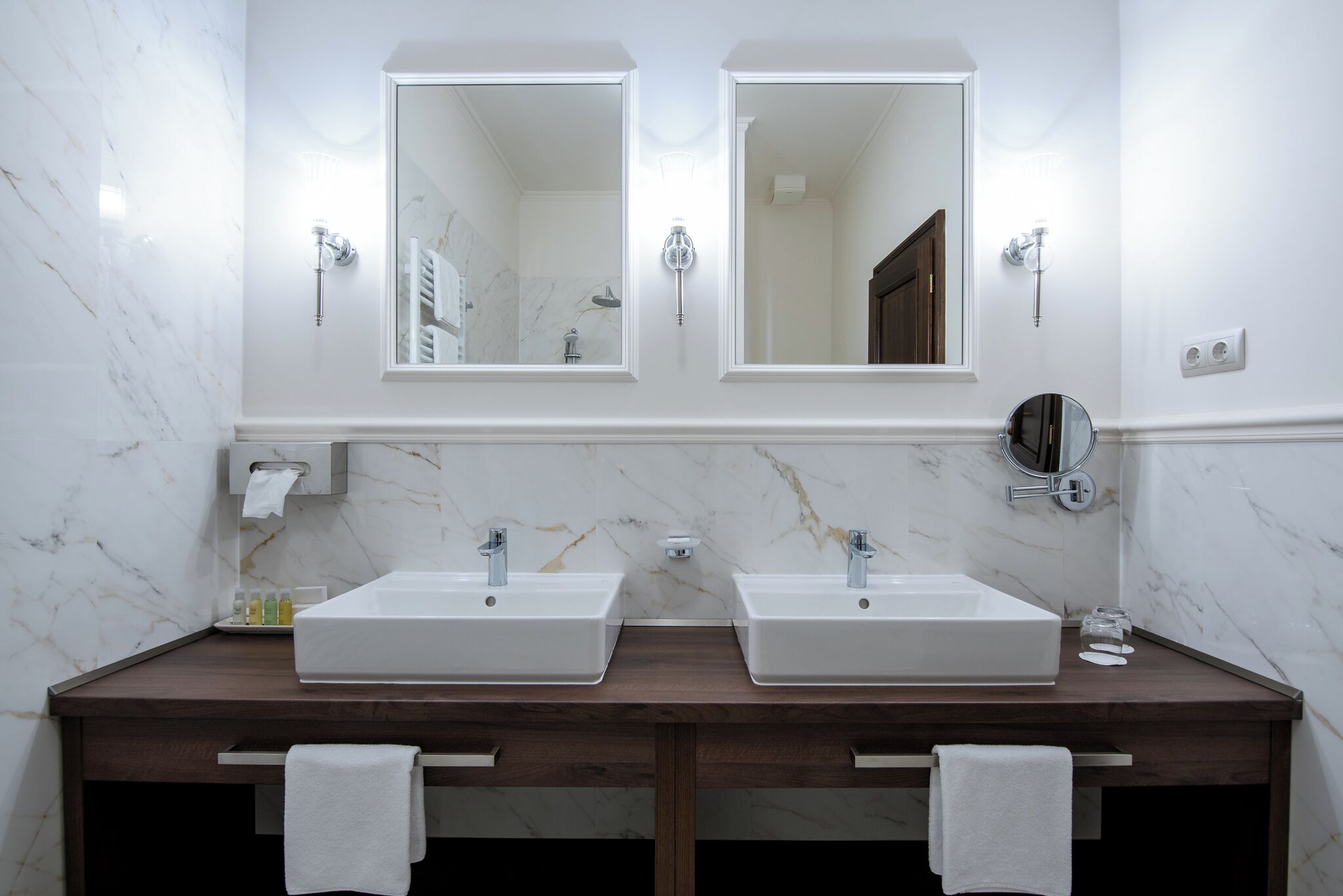 A bathroom with two sinks, marble walls, and a wooden vanity.