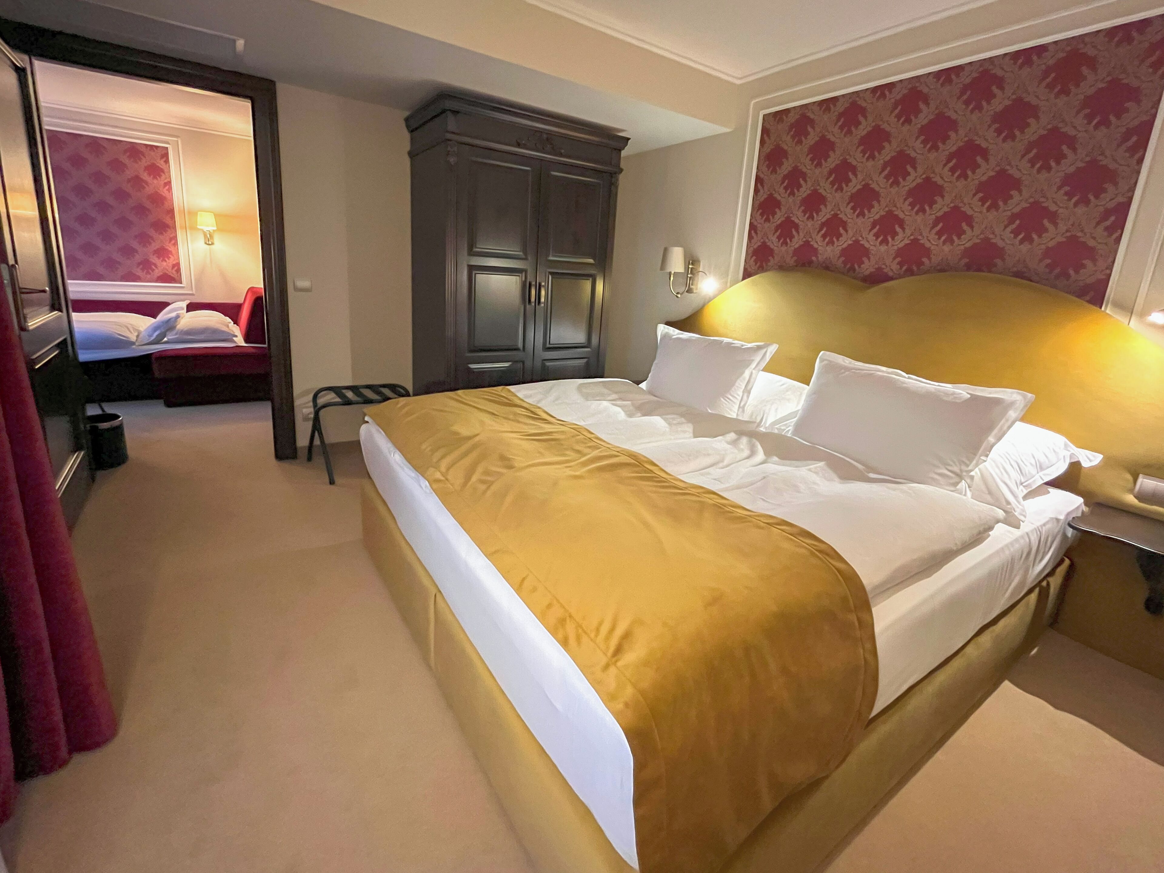 A hotel room with a large bed, a wardrobe, a desk with a lamp, and a chair.